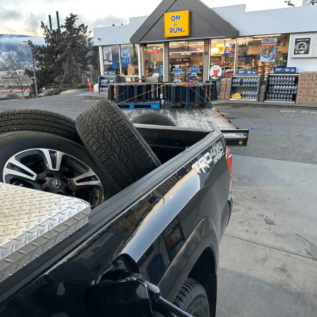 Black Toyota Tacoma pulling a flat deck trailer with LTL Freight in Kamloops, BC at an On-the-Run Gas station.